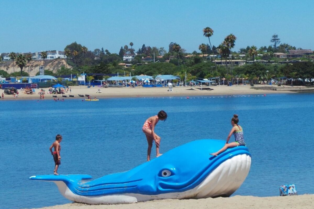 A giant blue floatable plastic whale on a beach with kids playing.