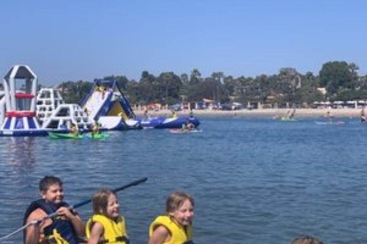 Four kids sitting on a stand up paddleboard with lifevests.
