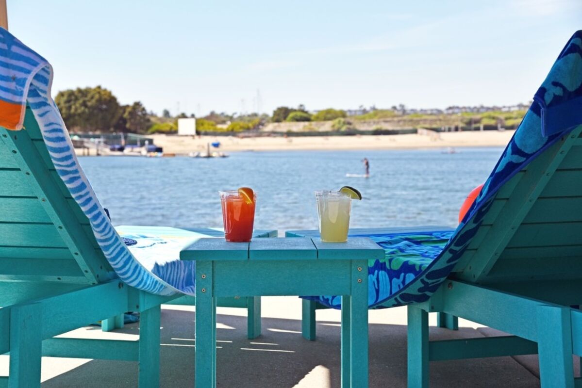 Beachside view of a waterfront lagoon with beach chairs and drinks.