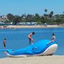 A giant blue floatable plastic whale on a beach with kids playing.